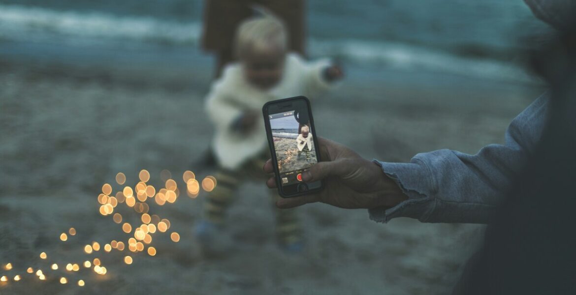 Limpieza de Armario Digital: Gestiona tus Recuerdo Mano grabando con un celular a un niño en la playa, simbolizando los recuerdos digitales que se deben organizar en una limpieza de armario digital para el bienestar mental.