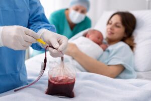 Profesional de salud recolectando sangre del cord&oacute;n umbilical tras el nacimiento mientras madre sostiene a su beb&eacute;